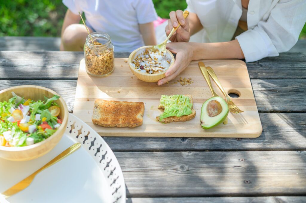 Crop woman and kid eating healthy breakfast breakfast in park