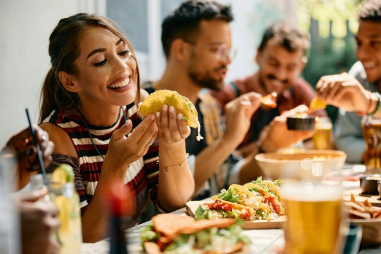 Happy woman eating tacos during a lunch with friends in Mexican restaurant.