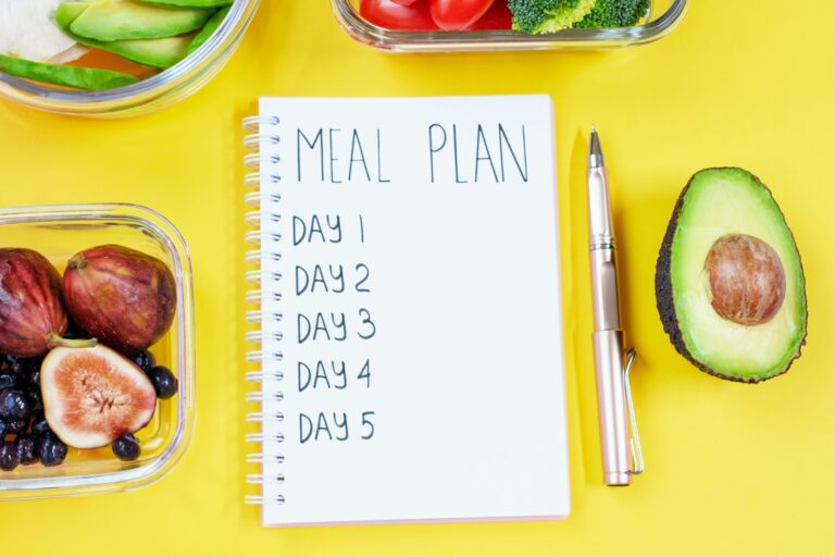 Notepad with inscription meal plan on yellow background and containers with food.